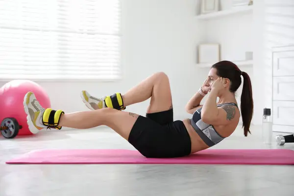 stock image Beautiful woman with ankle weights doing exercises indoors