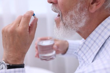 Bir bardak suyla evde hap alan yaşlı adam, yakın plan.