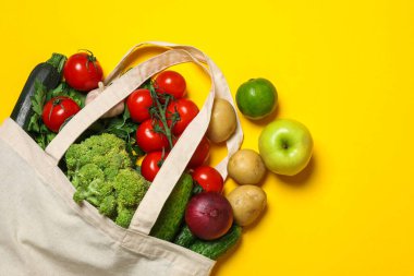 Vejetaryen ürünlerin teslimatı. Sarı arka planda farklı sebzeler ve meyvelerle dolu çantalar.
