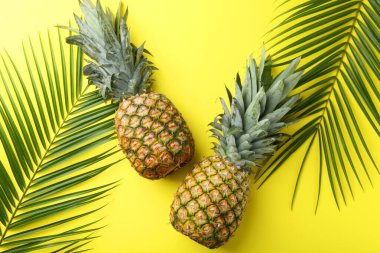 Sarı arka planda taze ananas ve palmiye yaprakları.