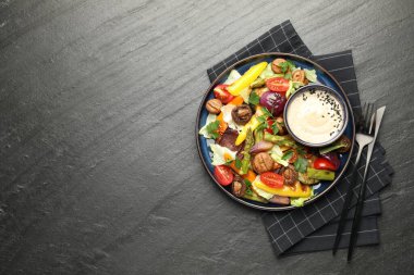 Koyu gri desenli masada servis edilen ızgara sebzeli ve soslu leziz salata. Metin için boşluk