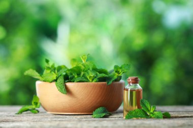 Bir şişe nane yağı ve ahşap masada taze yapraklar.