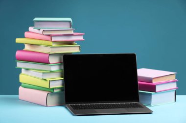Açık mavi arkaplanda renkli kitap ve dizüstü bilgisayar yığınları