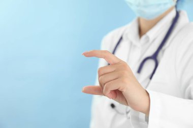 Doctor holding something on light blue background, closeup. Space for text
