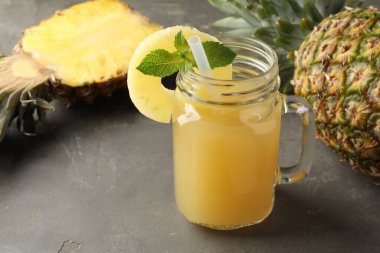 Mason kavanozunda nefis ananas suyu, gri desenli masada nane ve meyveler, yakın plan.