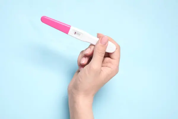 stock image Woman holding pregnancy test on light blue background, closeup