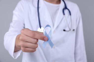 Prostat kanseri farkındalığı. Gri arkaplanda açık mavi kurdele tutan doktor, yakın plan.