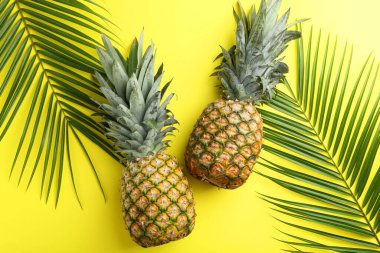 Sarı arka planda taze ananas ve palmiye yaprakları.