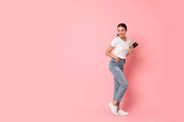 Pembe arka planda akıllı telefonu olan gülümseyen bir kadın. Metin için boşluk