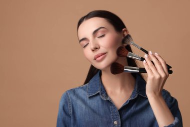 Güzel makyaj. Bej arka planda fırçaları olan çekici kadın, metin için boşluk