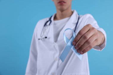 Prostat kanseri farkındalığı. Doktor, açık mavi kurdeleyi renk arkaplanı ve seçici odak üzerine desteğin sembolü olarak tutuyor