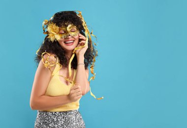 Karnaval maskesi takan mutlu genç bir kadın açık mavi arka planda, mesaj için yer var.