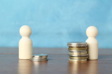 Finansal eşitsizlik. Masada açık mavi arkaplana karşı bozuk para ve ahşap figürler yığını