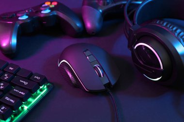 Bilgisayar faresi, kulaklık, RGB klavye ve oyun denetleyicileri koyu arkaplanda neon ışıkları, yakın plan