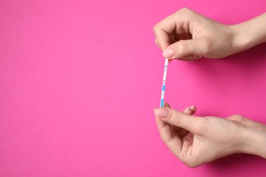 Pembe arka planda hamilelik testi yapan bir kadın. Metin için boşluk