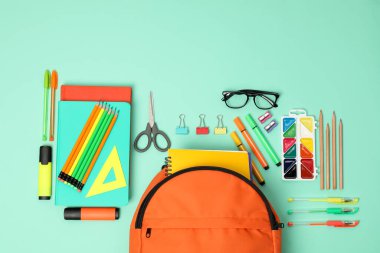 Sırt çantası ve turkuaz arka planda farklı okul malzemeleri.