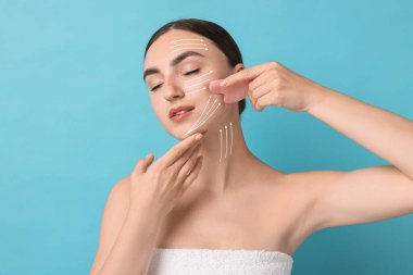 Güzel genç bir kadın açık mavi arka planda gua sha aletiyle yüz masajı yapıyor. Hareket yönlerini gösteren cilt üzerindeki çizgiler