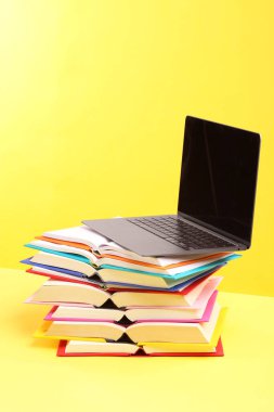 Sarı arkaplanda renkli kitap ve dizüstü bilgisayar yığını