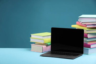 Açık mavi arkaplanda renkli kitap ve dizüstü bilgisayar yığını, metin için boşluk
