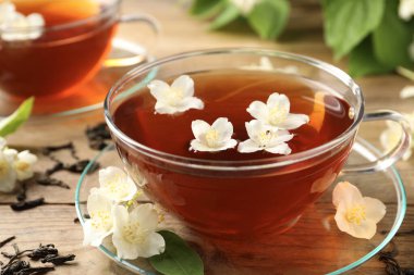 Sıcak yasemin çayı fincanda ve çiçekler ahşap masada, yakın plan.