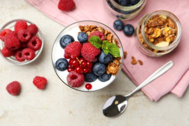 Taze böğürtlenli yoğurt, granola, bardakta nane ve gri desenli masada kaşık, düz uzanmış.