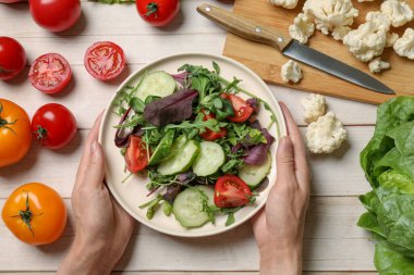 Sağlıklı vejetaryen yemekleri. Sebzeli, hafif ahşap masada salata tabağı tutan kadın.