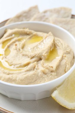 Kavanozda zeytinyağı ve beyaz masada limon olan lezzetli humus, yakın plan.