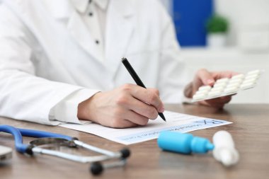 Klinikteki ahşap masada reçete yazan haplı doktor, yakın plan.