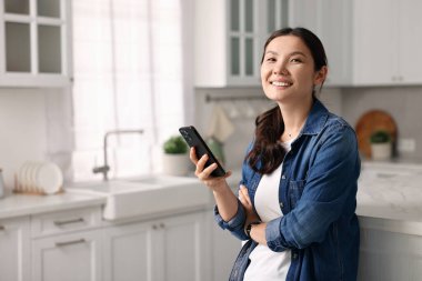 Mutfakta akıllı telefonu olan gülümseyen bir kadın. Metin için boşluk