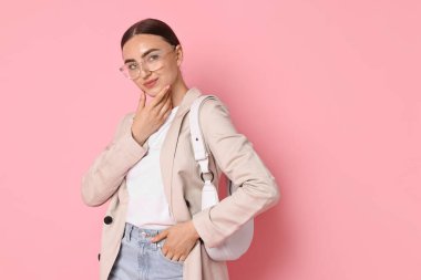 Pembe arka planda çantası olan bej ceketli şık bir kadın.