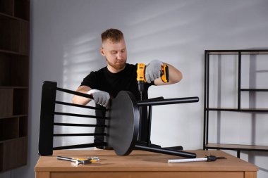 Elektrikli tornavidalı bir adam odada sandalye monte ediyor.