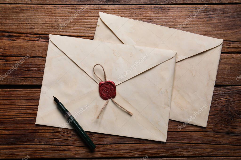 Old letter envelopes and pen on wooden table, top view