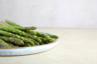 Taze yeşil kuşkonmaz tabağı açık dokulu masa üzerinde, yakın plan. Metin için boşluk