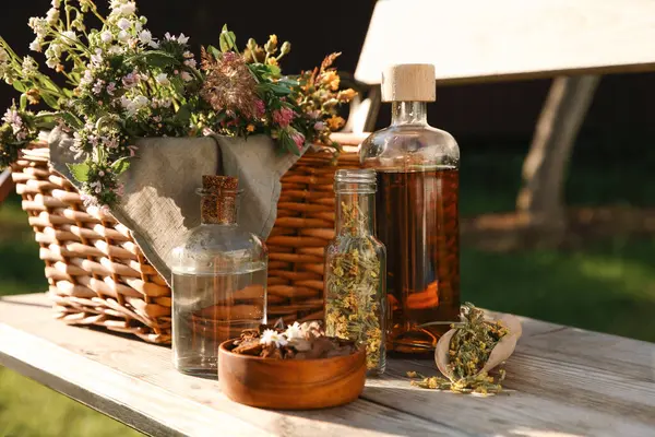 stock image Different tinctures in bottles, bark chips and flowers on wooden bench outdoors