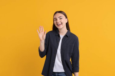 Turuncu arka planda el sallayan mutlu genç kadın