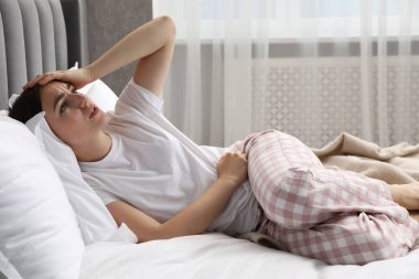 Evde, yatakta adet sancısı çeken bir kadın.