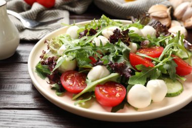 Lezzetli salata roka, marul, mozzarella peyniri ve sebzeler ahşap masada, yakın plan.