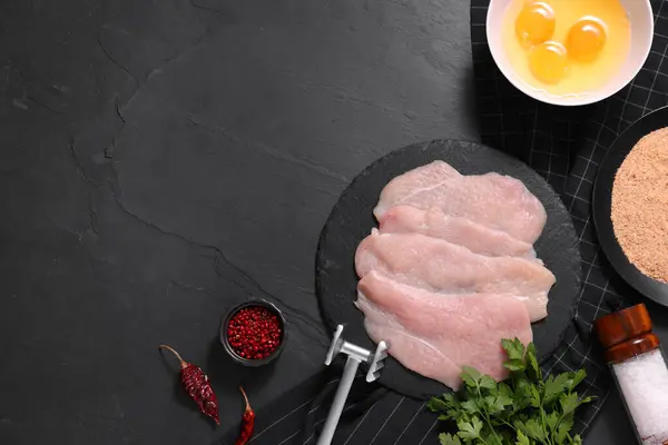 Stock image Making schnitzel. Raw meat chops, products and tenderizer on dark textured table, flat lay. Space for text