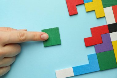 Açık mavi arka planda renkli ahşap yapboz parçalarıyla oynayan kadın, üst görünüm