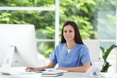 Hastane ofisinde bilgisayarla çalışan gülümseyen hemşire.