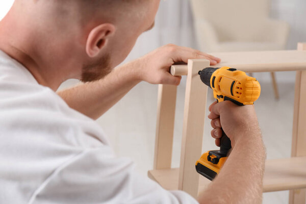 Man with electric screwdriver assembling furniture in room, closeup