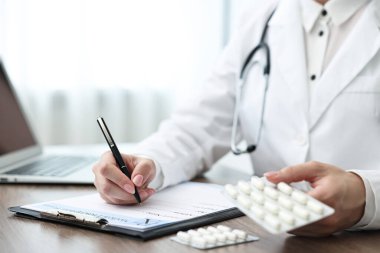 Klinikteki ahşap masada reçete yazan haplı doktor, yakın plan.