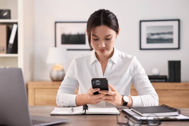 Ofisinde akıllı telefonu olan güzel bir iş kadını.