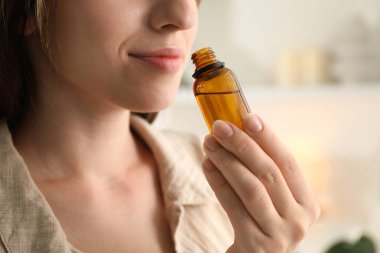 Woman with bottle of essential oil at home, closeup clipart