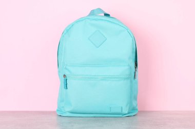 Açık mavi sırt çantası gri masada pembe arka planda
