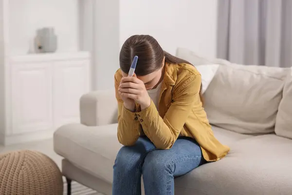 stock image Sad woman holding pregnancy test on sofa indoors, space for text