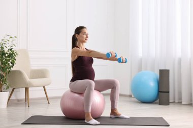 Kol halterli güzel hamile kadın evde spor yapıyor.