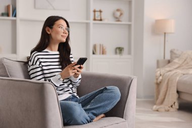 Evdeki koltukta akıllı telefonu olan güzel bir kadın.