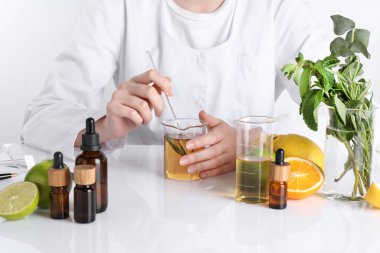 Aromaterapi ürünü. Bilim adamı laboratuarda, yakın planda, beyaz masada gerekli yağları geliştiriyor.