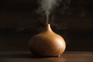 Aroma yağı yayıcı ve ahşap masa üzerinde buhar.